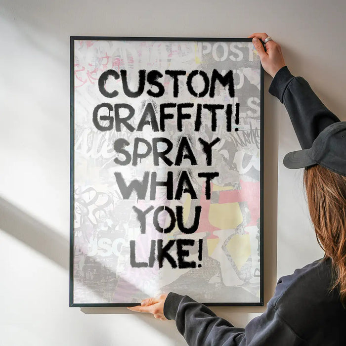 Hands holding a framed custom graffiti stencil print with black spray paint text "CUSTOM GRAFFITI! SPRAY WHAT YOU LIKE!