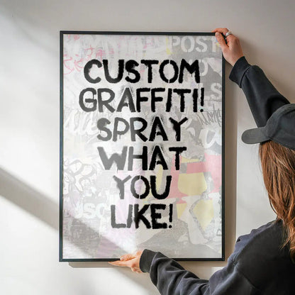 Hands holding a framed custom graffiti stencil print with black spray paint text "CUSTOM GRAFFITI! SPRAY WHAT YOU LIKE!
