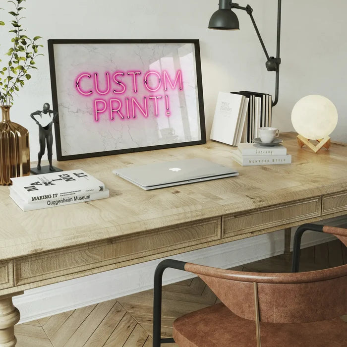 Framed custom neon print with pink "CUSTOM PRINT!" text on a white marble background, displayed on a wooden desk.