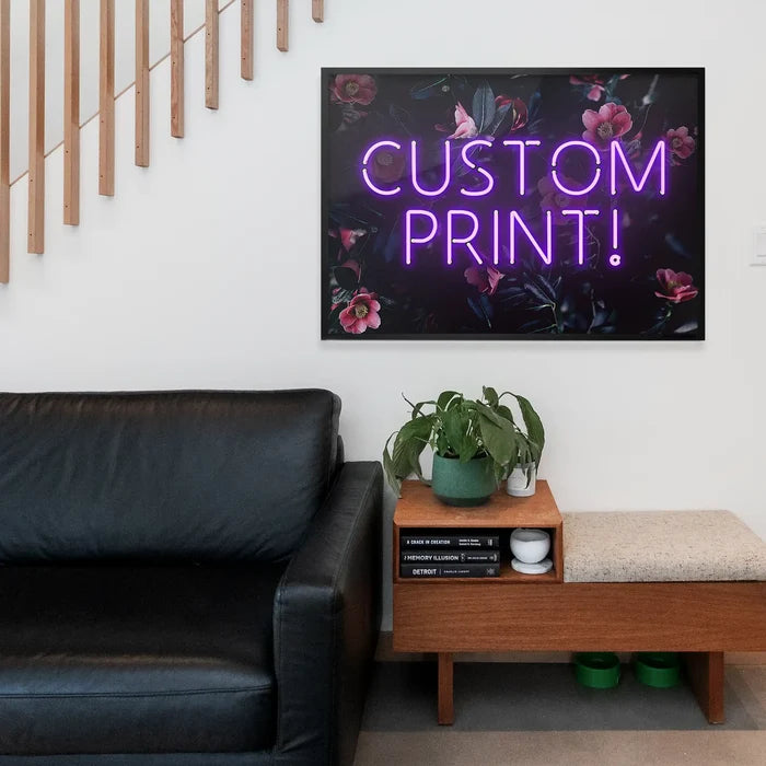 Purple neon "CUSTOM PRINT!" text on a dark floral background print, framed above a black leather sofa.
