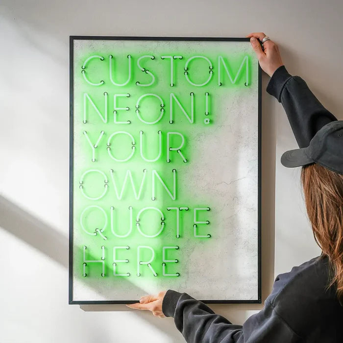 Hands hold a framed custom green neon print on a textured white background, reading "CUSTOM NEON! YOUR OWN QUOTE HERE.
