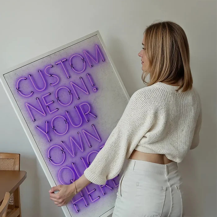 Woman holding a framed custom purple neon print with "CUSTOM NEON! YOUR OWN QUOTE HERE" text.
