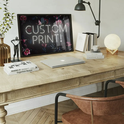Custom white neon sign print with "CUSTOM PRINT!" text on a dark floral background, displayed on a wooden desk.