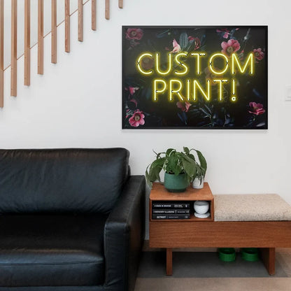 Yellow neon "CUSTOM PRINT!" text on a dark floral background print, framed above a black sofa.