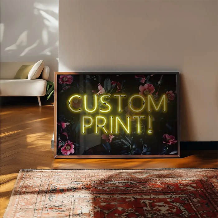 Custom yellow neon sign with "CUSTOM PRINT!" text on a dark floral background, framed, leaning on a wall.