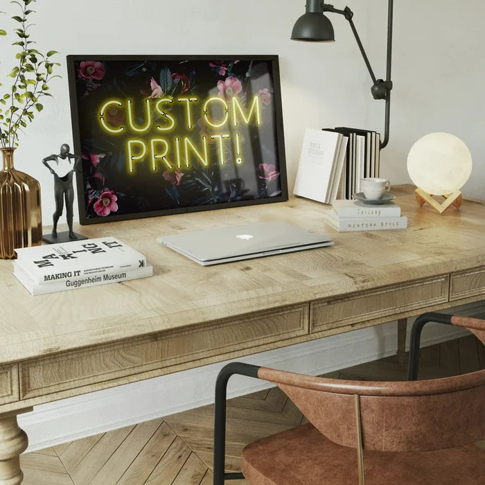 Custom yellow neon sign print with "CUSTOM PRINT!" text on a dark floral background, framed on a wooden desk.