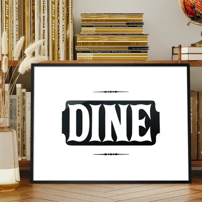 Black framed "DINE" typographic print on white archival paper, displayed on a wooden shelf.