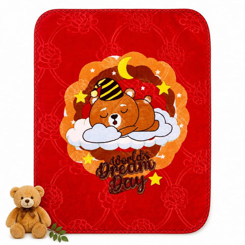 A red plush blanket with rounded corners featuring a cartoon bear sleeping on a cloud with the text 'World's Dream Day' and a crescent moon and stars. A small teddy bear and green leaves are placed at the bottom left on a white background.