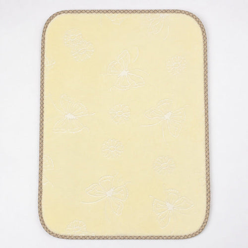A pale yellow rectangular mat with rounded corners, featuring a subtle white embroidered butterfly and floral pattern and a braided tan border, shown on a plain white background.