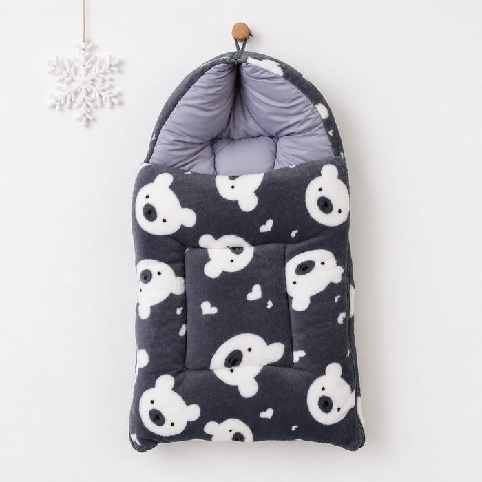 A quilted baby footmuff in dark gray with a white teddy bear pattern, hanging from a wooden peg on a white wall next to a white snowflake ornament.