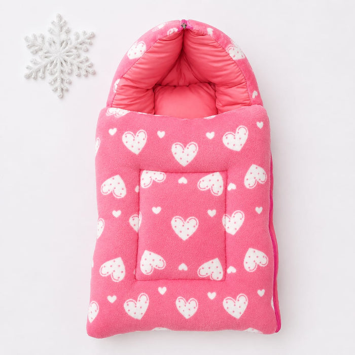 A pink quilted baby bootie or foot warmer with a white heart pattern, shown flat on a white background next to a white decorative snowflake ornament.