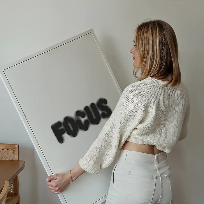 Woman holding a white framed "FOCUS" typographic art print with bold, black 3D-style lettering.