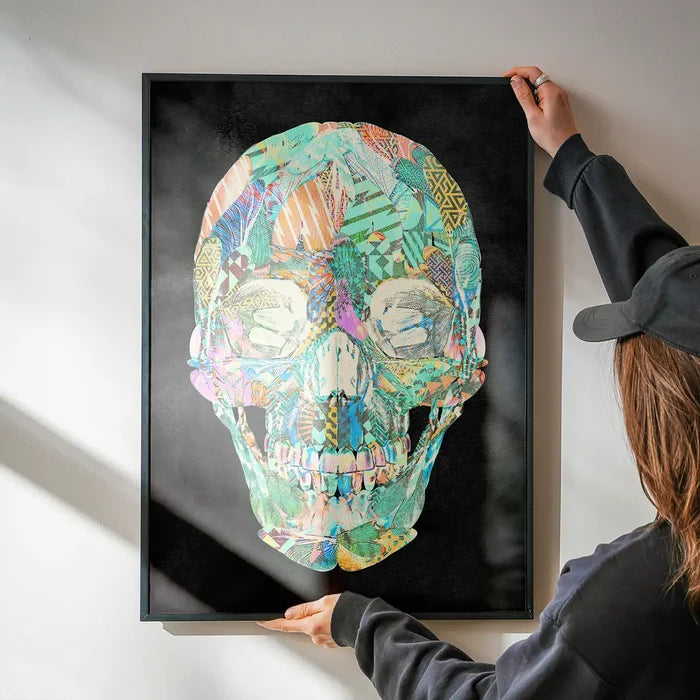 Person hanging a framed geometric pastel pattern skull print on a white wall.