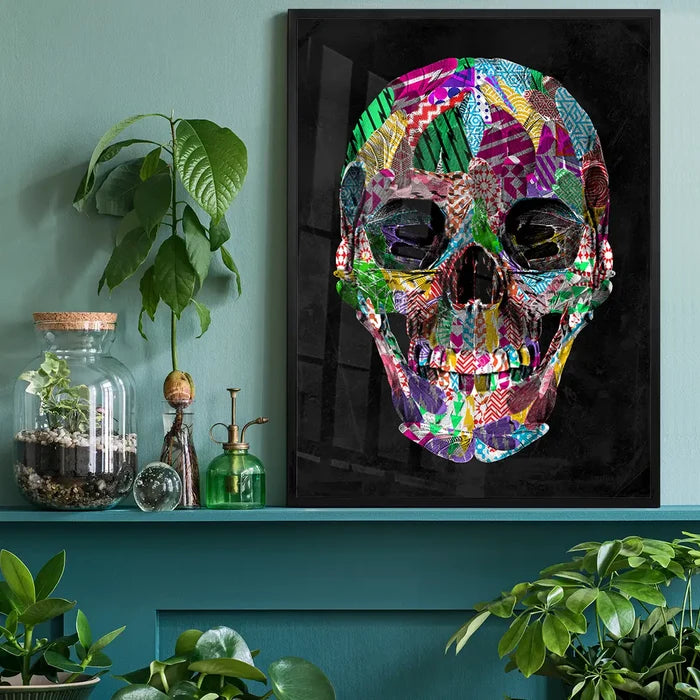 Bold, colorful geometric skull art print in a black frame, displayed on a teal shelf with plants.