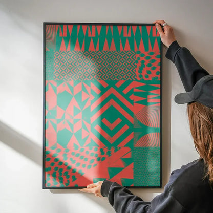 Hands hanging a framed pink and green abstract geometric print on a white wall.