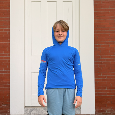 Child wearing a blue hoodie and gray shorts standing on steps with a white door and brick wall in the background.