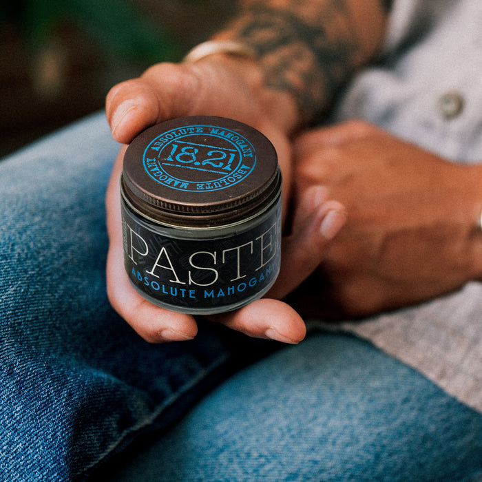 Hand holding a jar of 18.21 Paste Absolute Mahogany against a blurred background