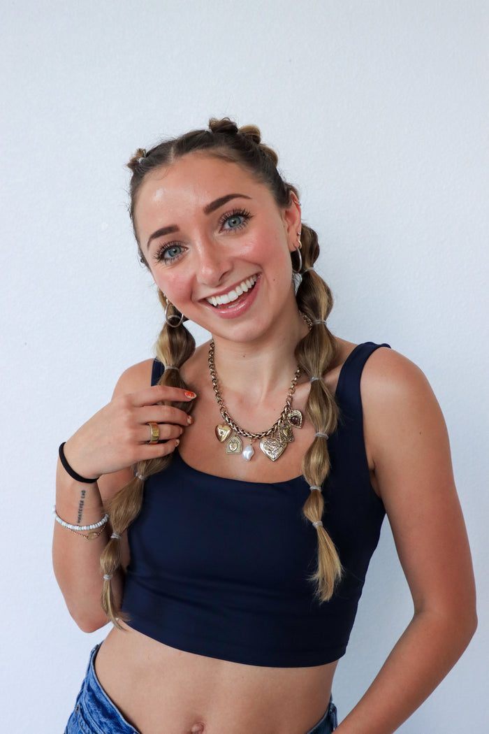 Woman with braided hair wearing a black top and denim shorts against a white background