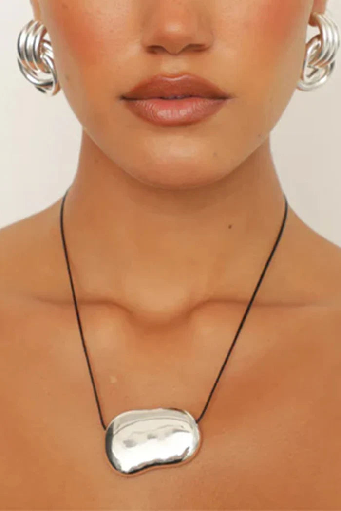 Close-up of a person wearing a silver necklace and earrings on a plain background