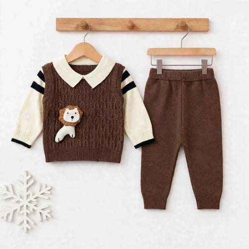 A baby clothing set displayed on wooden hangers against a light background. The set includes a brown cable-knit vest with cream sleeves, black sleeve stripes, a cream collar, and a small lion applique on the chest, paired with matching brown pants.