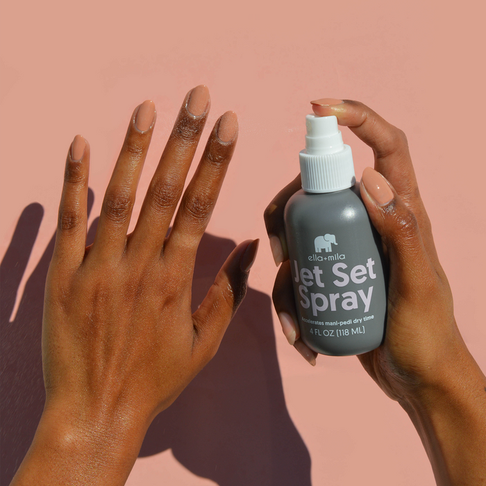 Spraying Jet Set Spray over a manicure on a medium skin tone, peach background