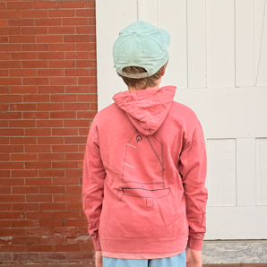 Person wearing a pink hoodie and blue shorts standing on steps with a brick wall and white door in the background.