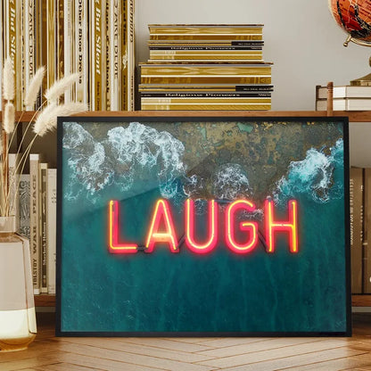 Framed wall art featuring a vibrant red neon LAUGH sign layered over an aerial ocean wave print on glossy paper.