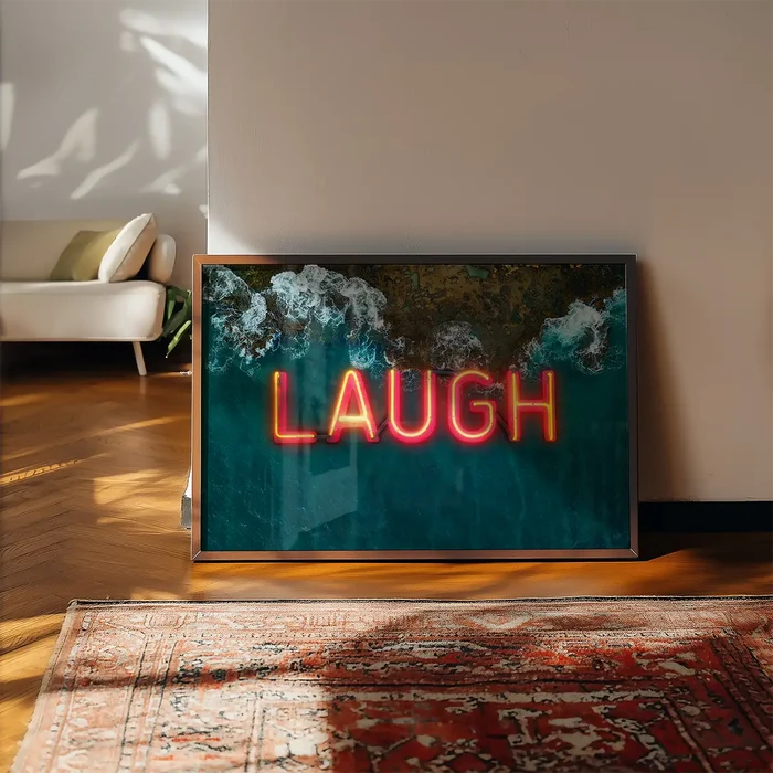 Glossy framed print featuring a bright red neon LAUGH sign set against a vibrant aerial ocean wave backdrop on a wooden floor.