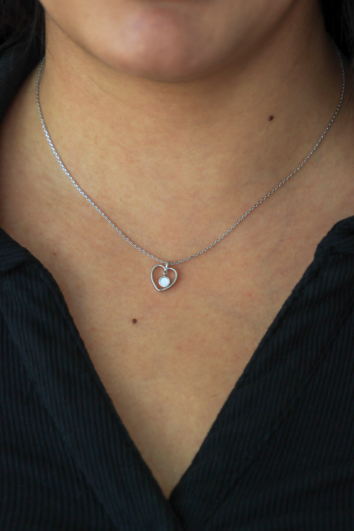 Silver necklace with a heart-shaped pendant worn by a person against a black background