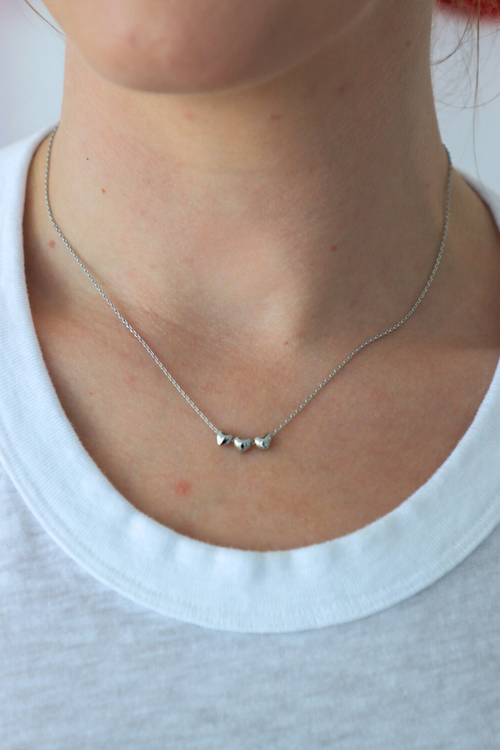 Silver necklace with small pendants on a person wearing a white shirt.