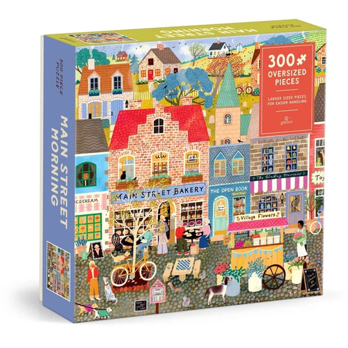 The Galison Main Street Morning 300 Piece Jigsaw Puzzle features a cozy and charming illustration of bustling shops, friendly people, and playful animals along a lively town street. The puzzle includes 300 oversized pieces for easy handling.