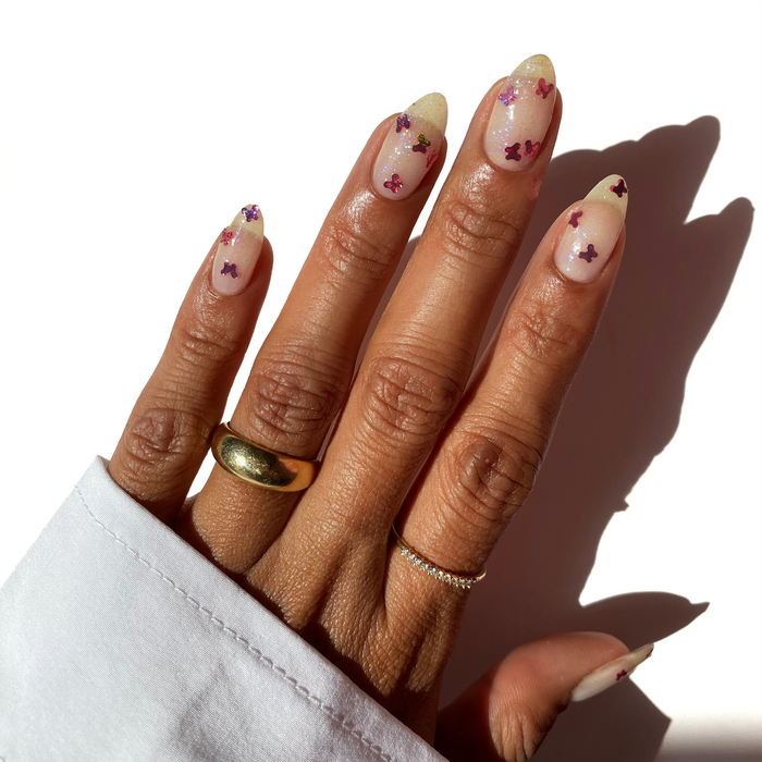 New Beginnings pink butterfly glitter over a sheer nude manicure with gold rings