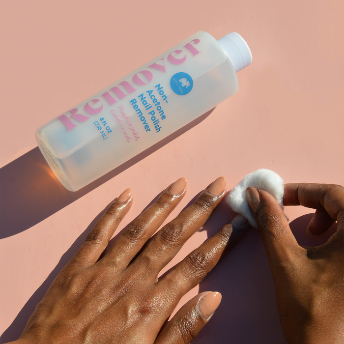 Removing polish with a cotton pad beside the Non-Acetone Nail Polish Remover bottle, peach background
