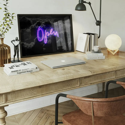 Framed purple neon Open script print on dark clouds, displayed on a wooden desk with modern office decor.
