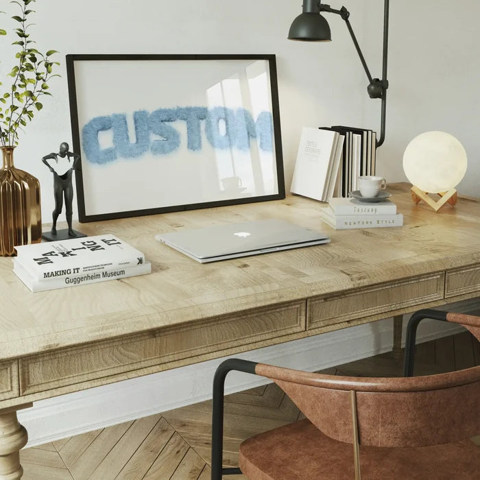Pastel blue fur-style "CUSTOM" name print in a black frame on a wooden desk with a laptop and decor.