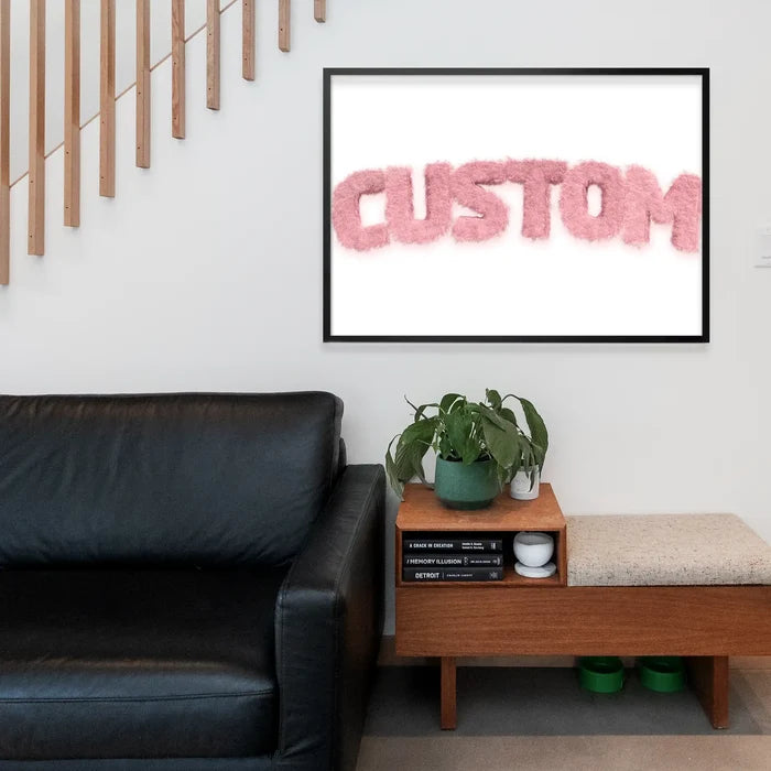 Framed pastel pink fur-style "CUSTOM" name print above a black sofa and wooden bench.