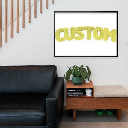 Pastel yellow fur style personalized name print in a black frame above a black leather sofa.