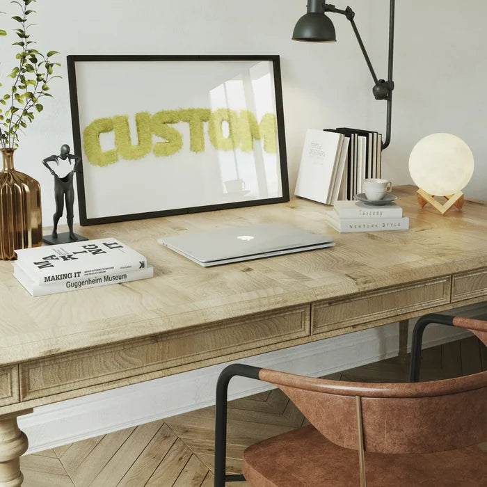 Pastel yellow fur-style "CUSTOM" name print in a black frame on a wooden desk with a laptop and decor.