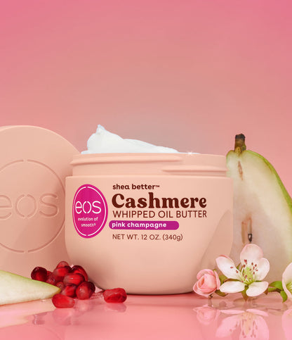 Eos Cashmere Whipped Oil Butter jar with pears, flowers, and pomegranates on a pink background
