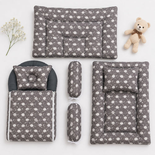 A baby bedding set arranged on a white background, including a changing pad, mattress, footmuff, two cylindrical bolsters, and a matching pillow, all in a gray fabric with a white cloud pattern. A small teddy bear and baby's breath sprig are placed as sty