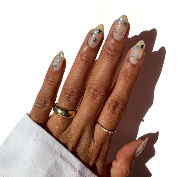 Rise and Fly teal butterfly glitter over a sheer nude manicure with gold rings