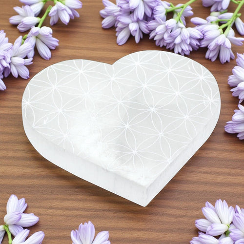 Heart-shaped selenite charging plate on a wooden surface with purple flowers