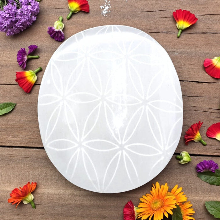 White Selenite plamstone with floral pattern on a wooden surface with colorful flowers.