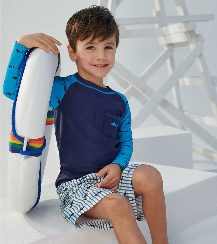 Boy sitting in Hatley shark swim trunks with matching blue swim top
