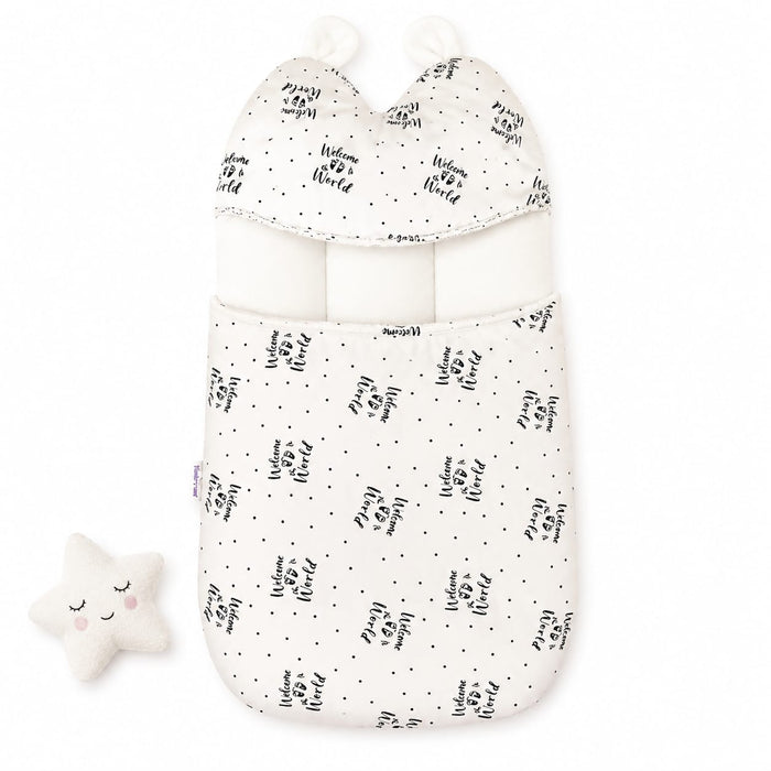A baby sleep bag or swaddle in warm off-white fabric with a black hand-lettered 'Happy Birthday' print and small black dots, shown on a white background with a matching plush star toy.