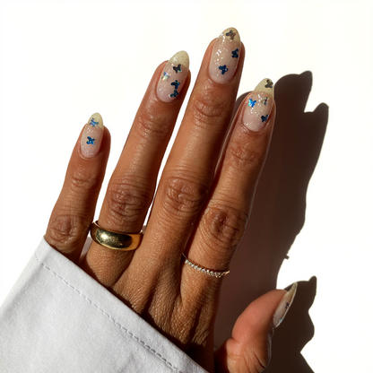Silver Skyline blue butterfly glitter over a sheer nude manicure with gold rings