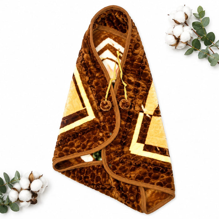 A brown textured hooded blanket or throw with cream and dark brown geometric patterns, laid flat on a white background with decorative cotton and eucalyptus sprigs in the corners.