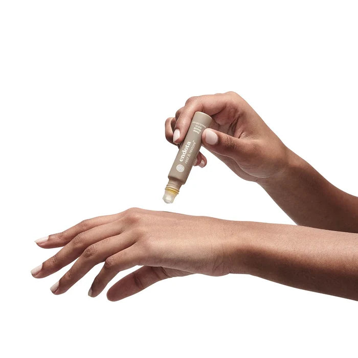 Hand applying endota sleep sound essential oil rollerball to another hand on a white background