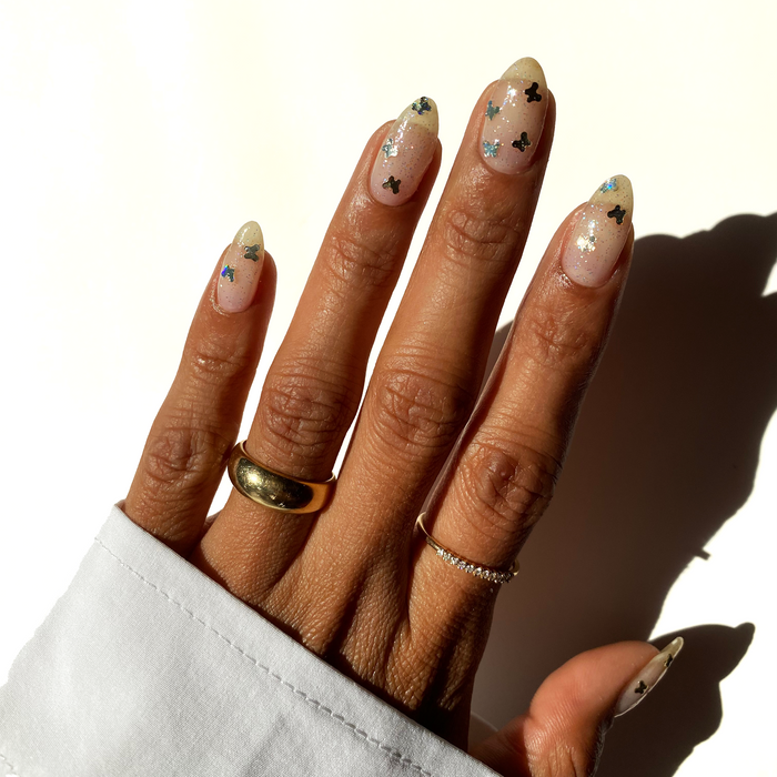 Soar with Grace gold butterfly glitter over a sheer nude manicure with gold rings