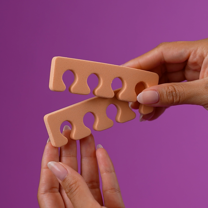 Hand holding a peach foam toe separator on a purple background